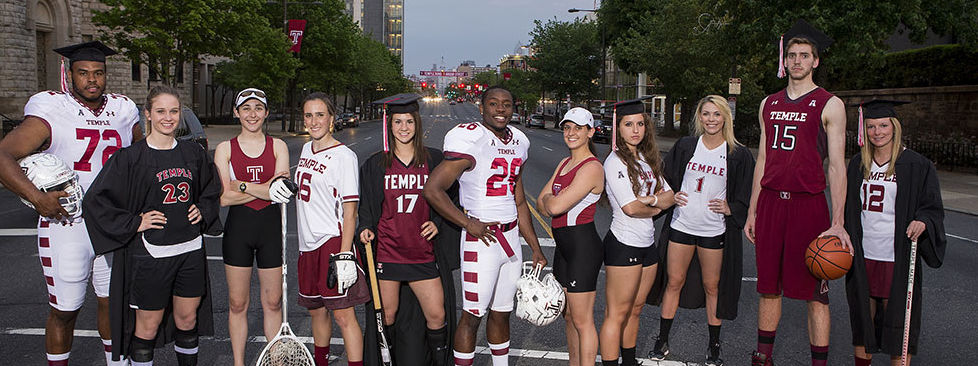 Men and women athletes in Temple University uniforms stand in a line on a city street